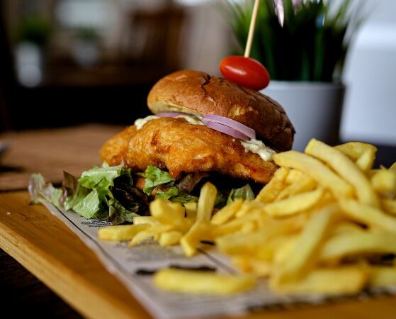 Hamburguesa de pollo frito con mayonesa de pesto, cebolla roja y patatas fritas.